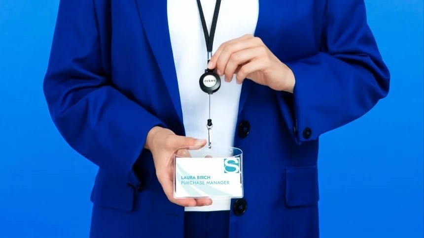 A man in a blue suit with a lanyard with a name tag around his neck