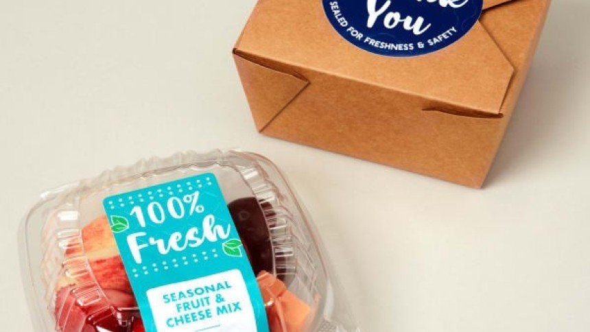 A small container of fresh fruit with a "100% Fresh" label, next to a brown takeout box sealed with a blue "Thank You" tamper-evident sticker.