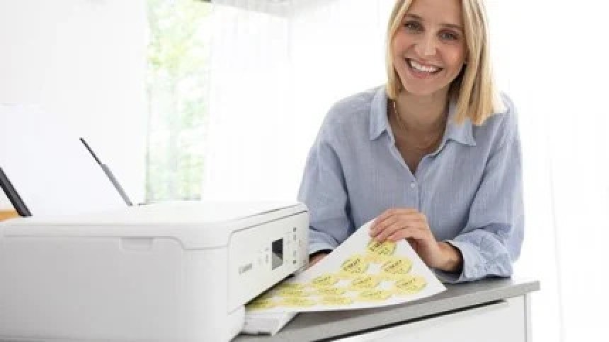 A smiling woman holds a sheet of round, yellow labels she has just printed on her home office printer.