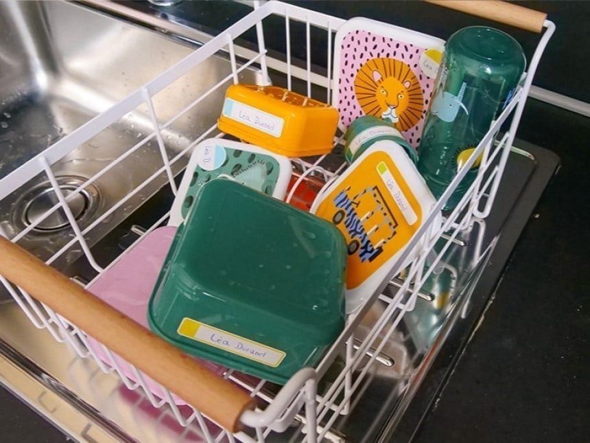 A metal basket suspended above the sink, containing various plastic breakfast dishes and a water bottle with a children's motif.