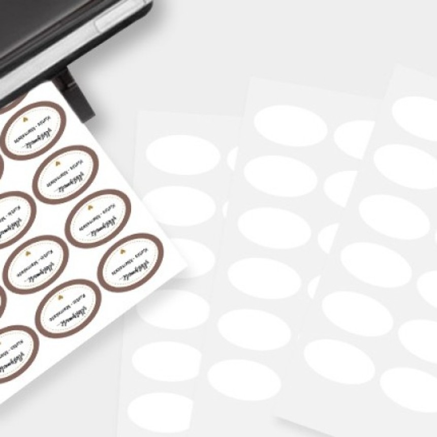 A printer producing a sheet of oval labels, some printed with brown borders and text, while blank oval label sheets lie next to it on a light gray background.
