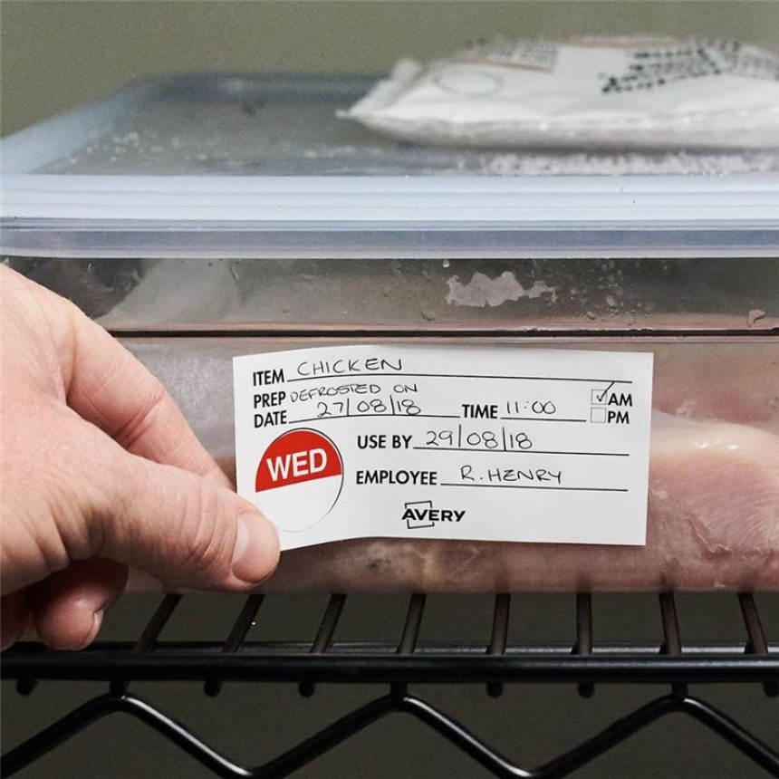 A person applies an Avery food safety label to a container of raw chicken on a wire shelf. The handwritten label reads: "Item: Chicken, Date: 27/08/18, Time: 11:00 AM, Use by: 29/08/18, Employee: R. Henry." A red "WED" sticker is on the left.