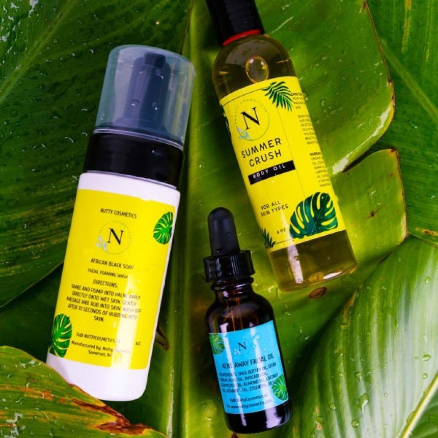 Three products from Nutty Cosmetics: a facial cleanser, “Summer Crush” body oil, and facial oil. The products are displayed on a large, lush green leaf, suggesting their natural ingredients.