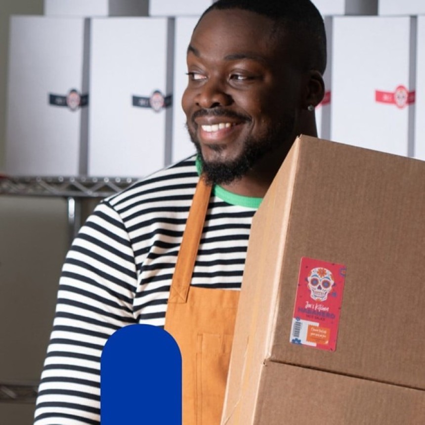 A smiling man in an apron holds a cardboard box with a colorful shipping label.