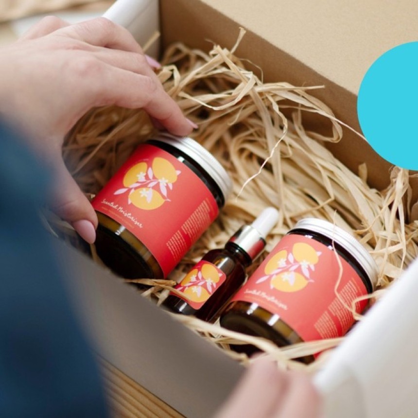 Hands arranging a set of cosmetics with custom labels in a box with filler.